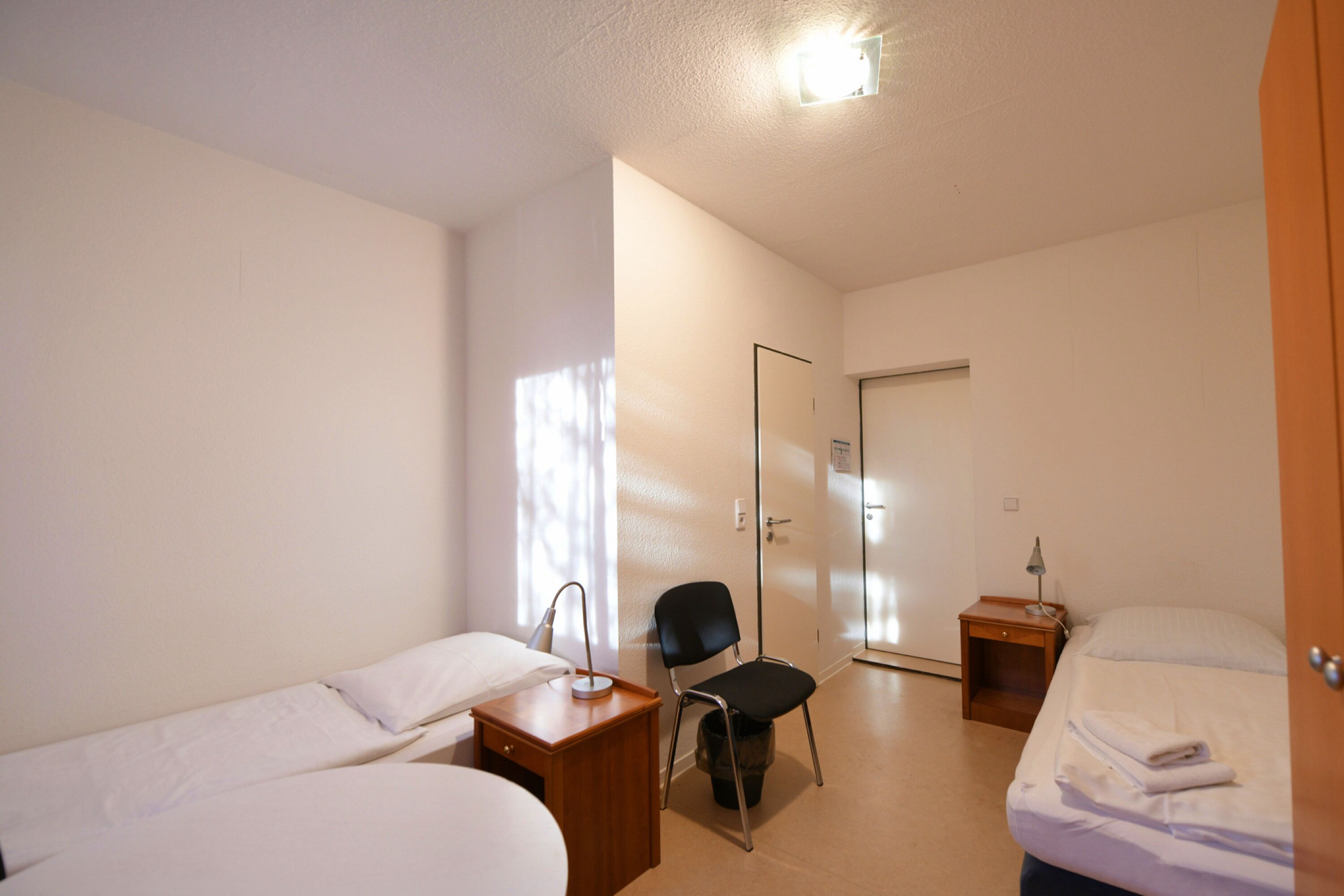 Een hotelkamer met twee eenpersoonsbedden, een stoel, een bureau met een lamp en een kledingkast.