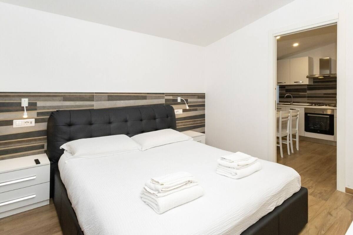 Ein modernes Schlafzimmer mit einem großen Bett, Nachttischen und Blick in einen Küchenbereich.
