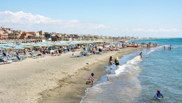 Une plage bondée, avec de nombreux transats et parasols, une étendue de sable et, en arrière-plan, une vue sur la ville.
