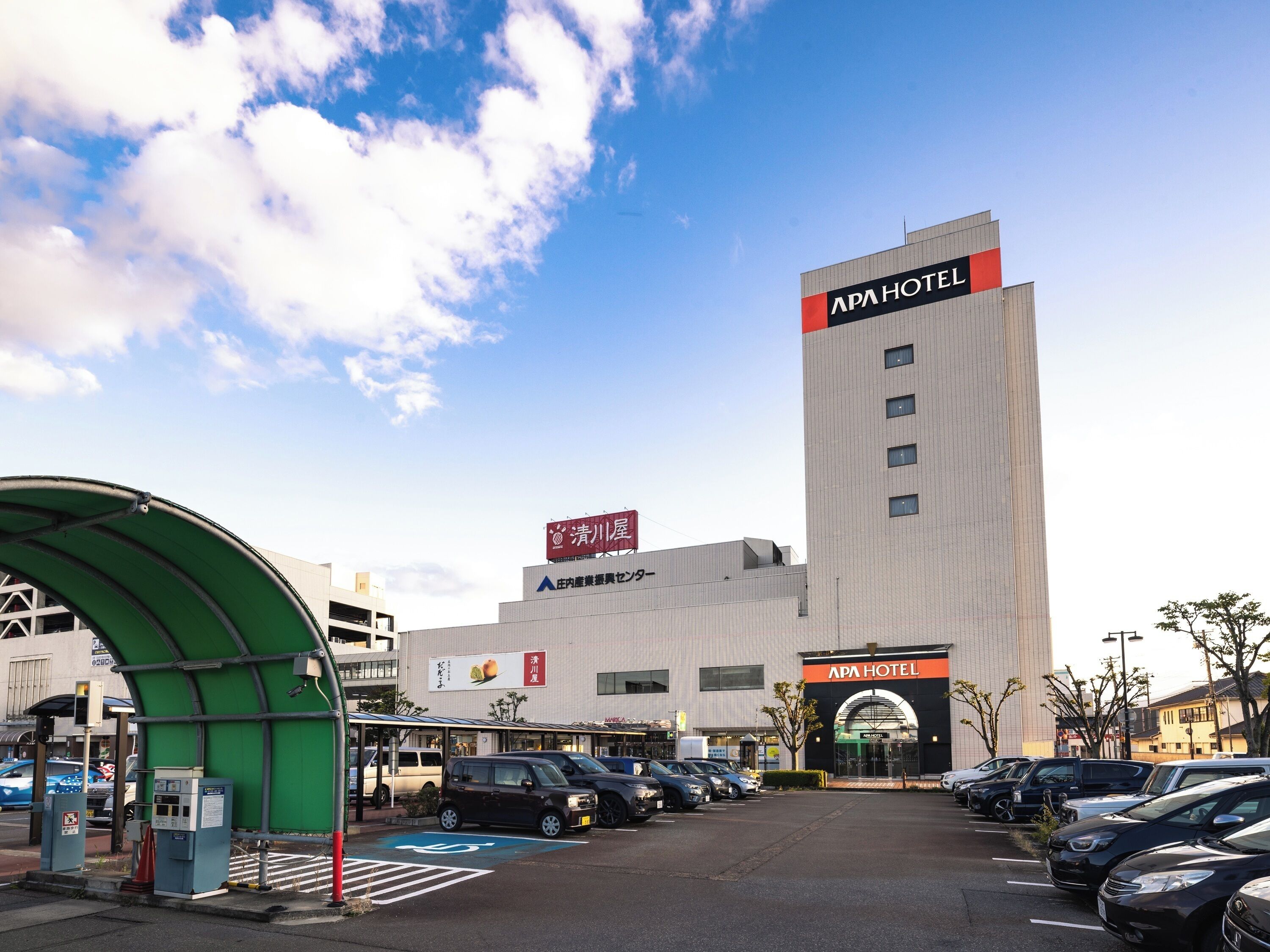 Een hotel met een opvallend bord, een parkeerplaats en een groene constructie op de voorgrond.