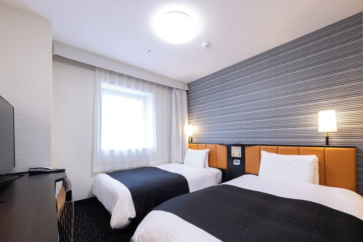 Ein Hotelzimmer mit zwei Betten, einem Schreibtisch und einem großen Fenster.