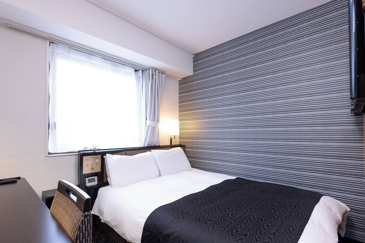 Ein Hotelzimmer mit einem Bett, einem Schreibtisch und einem fensterbepflanzten Fenster.