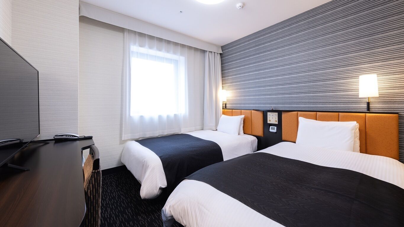 Habitación de hotel con dos camas, un escritorio con computadora y un ventanal con cortinas.