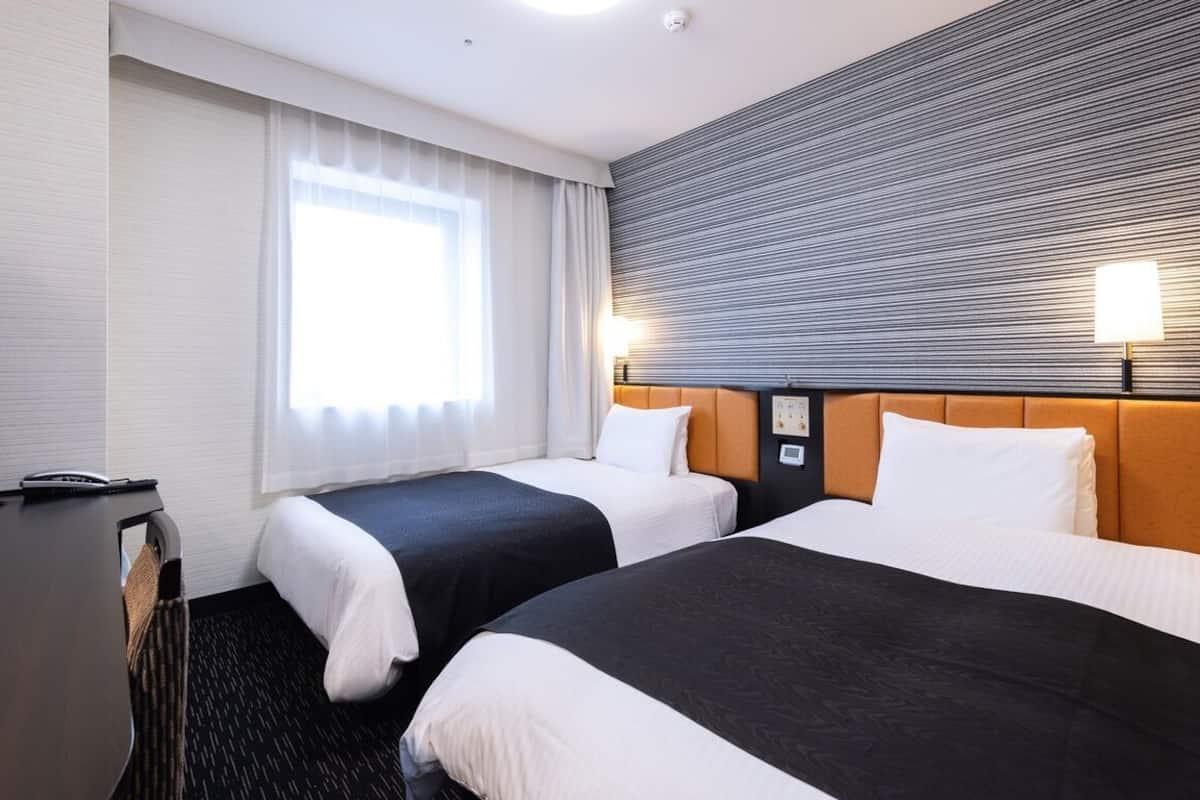 Une chambre d’hôtel avec deux lits, un bureau avec un ordinateur et une grande fenêtre avec des rideaux.