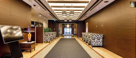 A hotel lobby with a long carpeted corridor, wooden panel walls, and a reception desk with a TV.