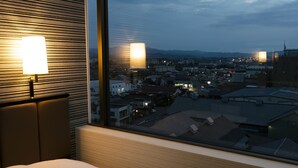 Ein Hotelzimmer mit großem Fenster und Blick auf die Stadt im Abenddämmerung.