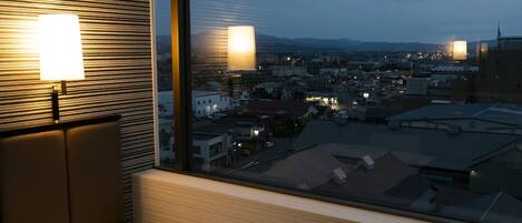 Habitación de hotel con un amplio ventanal que ofrece vistas a la ciudad al anochecer.