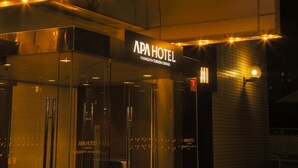 Das äußere Erscheinungsbild des APA Hotels mit beleuchteter Beschilderung und einem Glastür-Eingang.