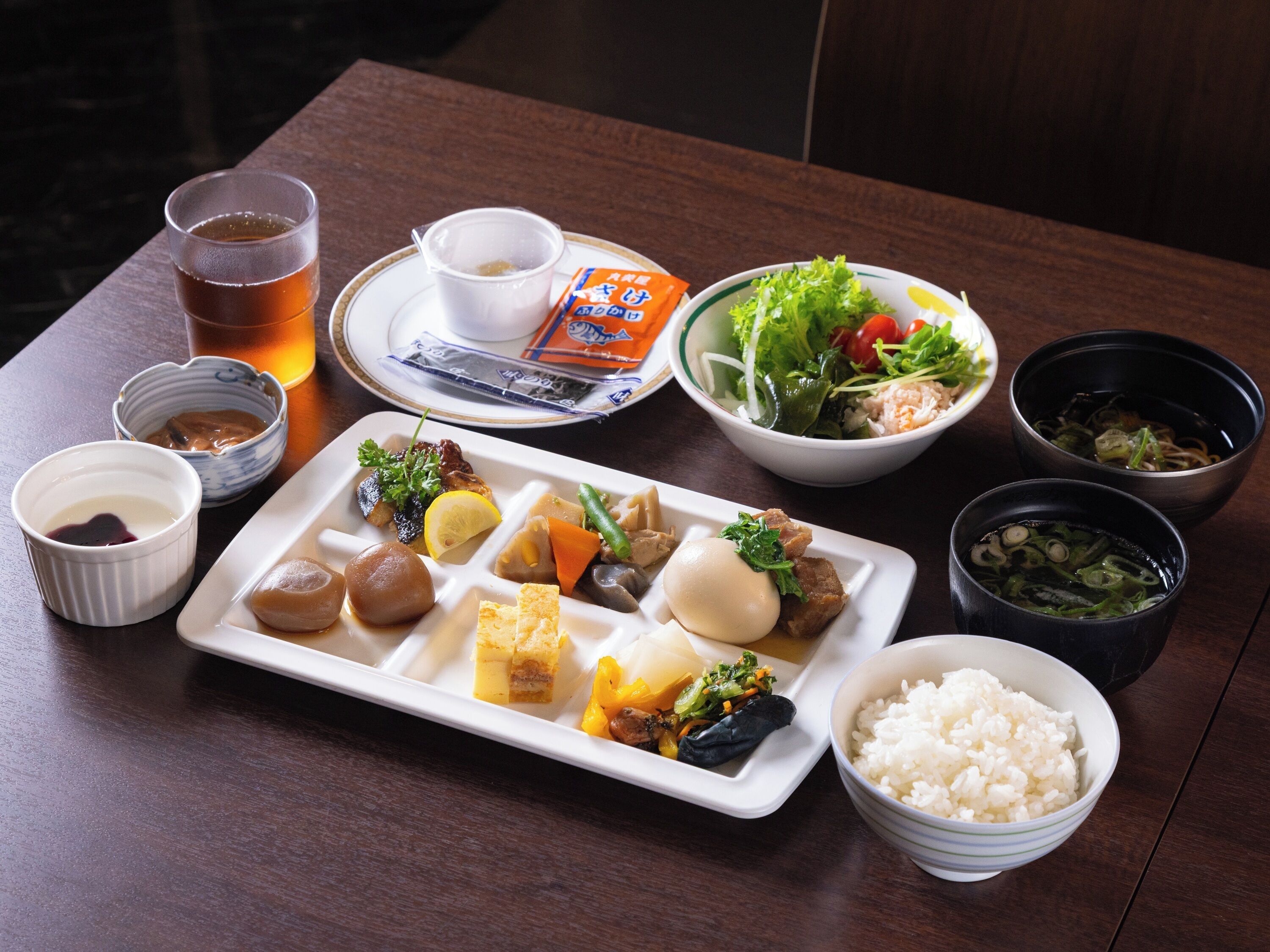 Une table où l’on trouve divers plats, notamment du riz, une soupe et une salade.