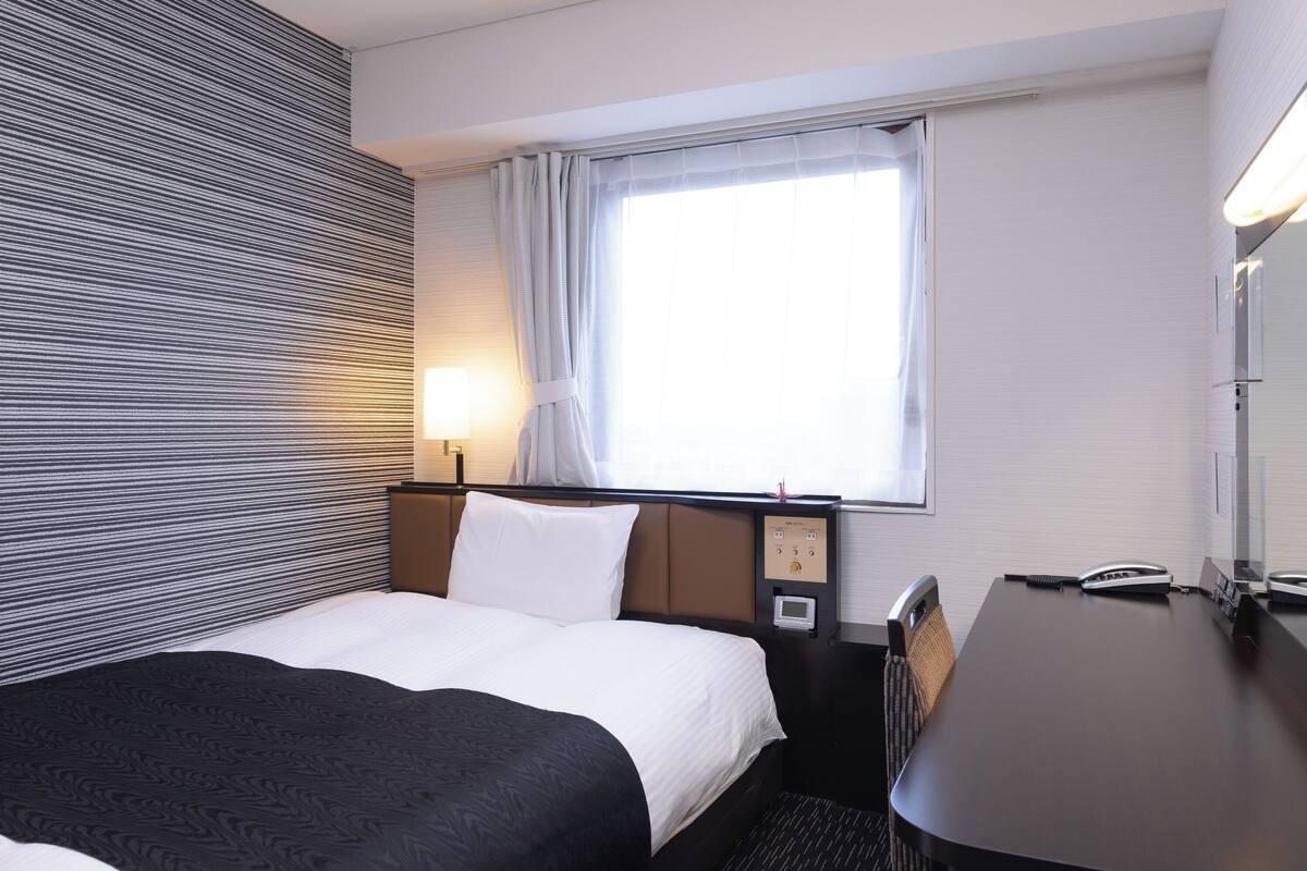 Ein Hotelzimmer mit Bett, Schreibtisch und einem Vorhangfenster.