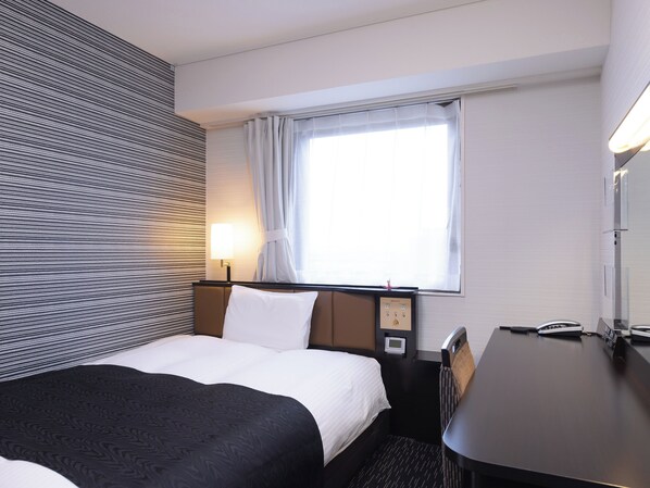 A hotel room with a bed, a desk, and a window with curtains.