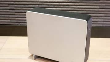 A modern, minimalist air purifier with a sleek design, placed on a wooden floor against a textured wall.