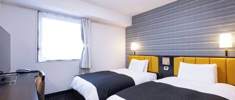Ein Hotelzimmer mit zwei Betten, einem Schreibtisch und einem Fenster mit Vorhängen.