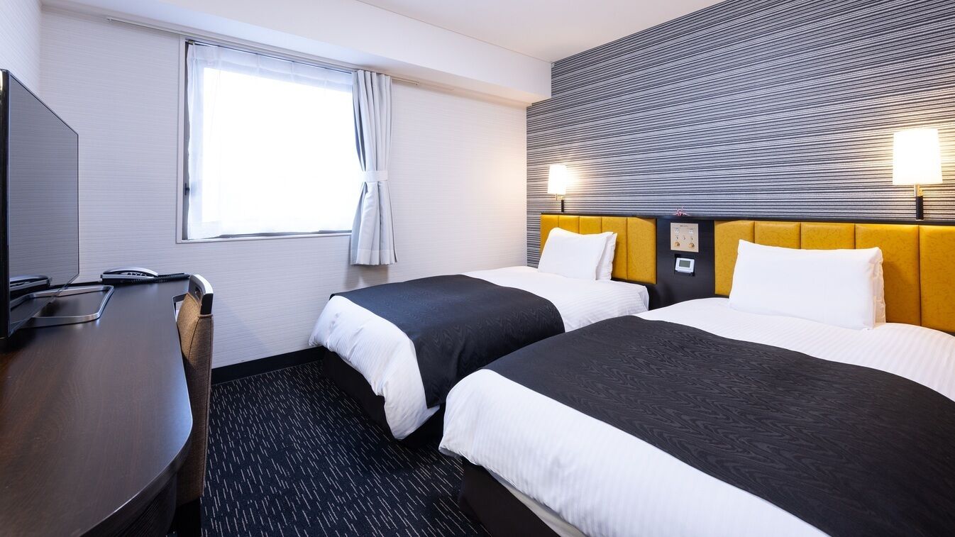 Una habitación de hotel con dos camas, un escritorio, un televisor y una ventana con cortinas.