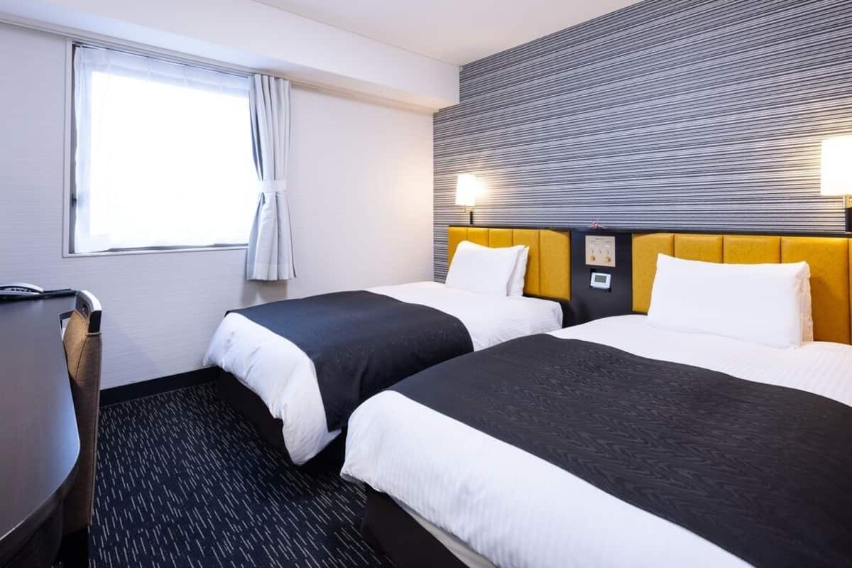 Une chambre d’hôtel avec deux lits, un bureau, une télévision et une fenêtre avec des rideaux.