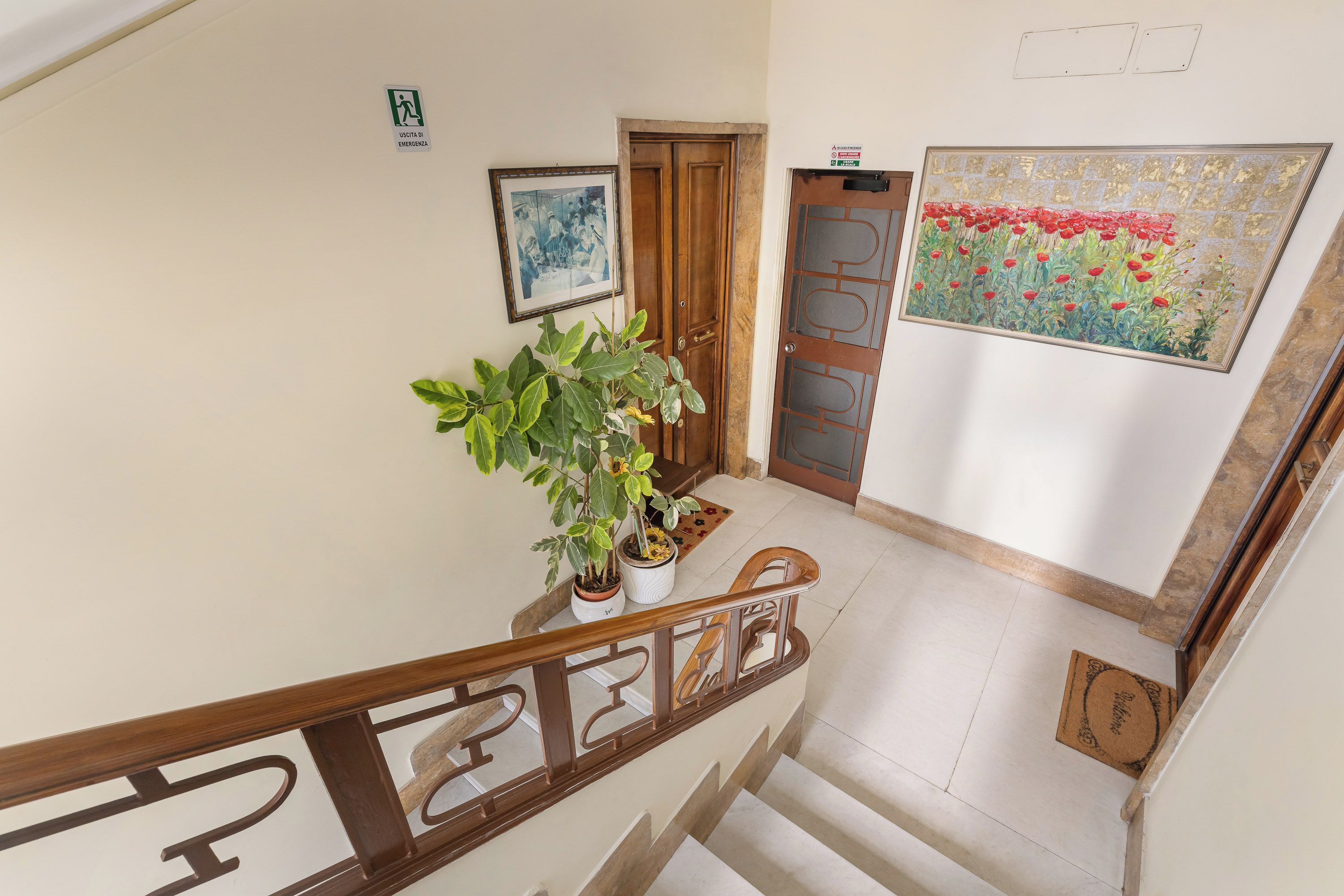 Una escalera con barandilla de madera, una planta en maceta y una puerta con panel de vidrio.