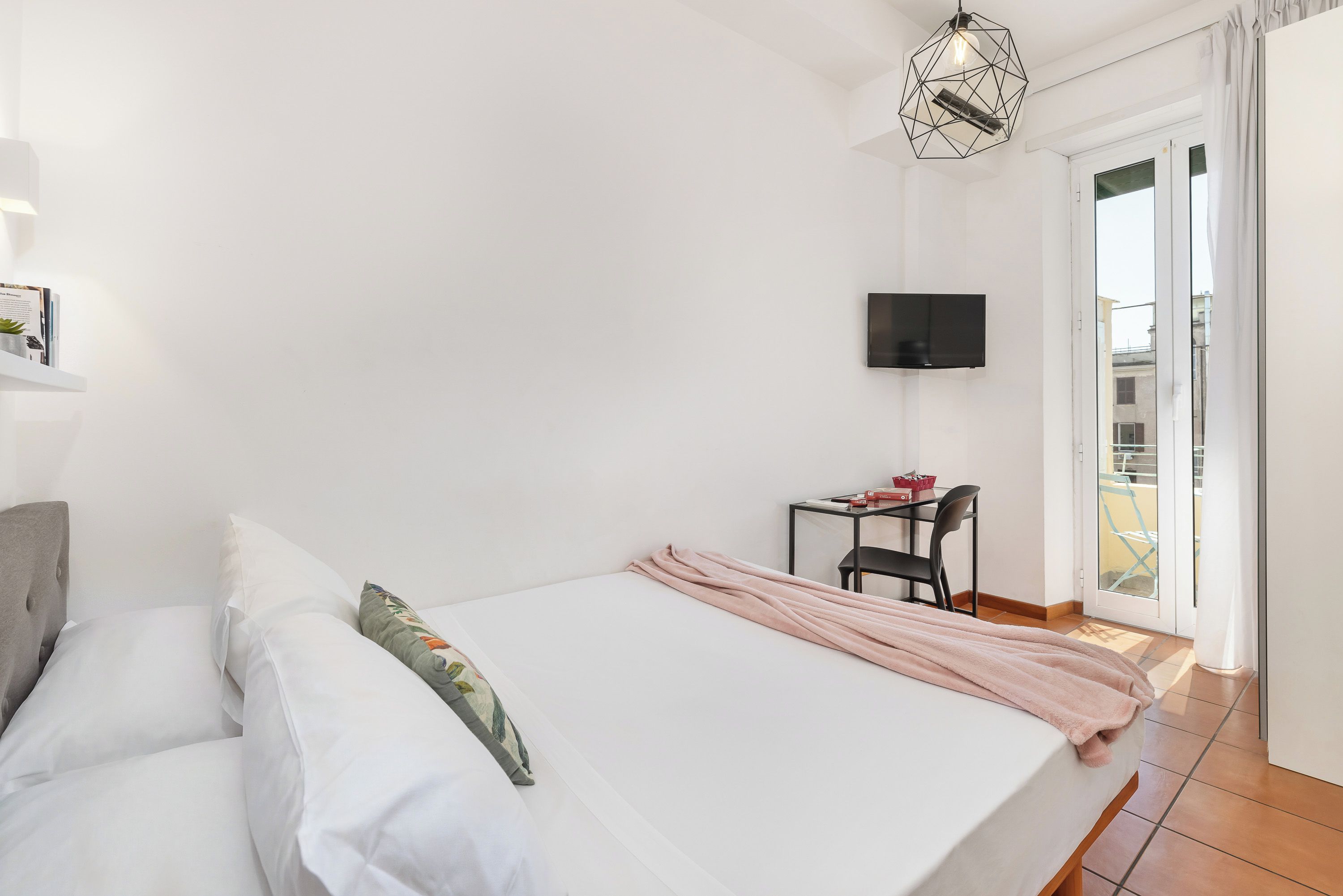 A bedroom with a bed, a desk, a television, and a balcony.