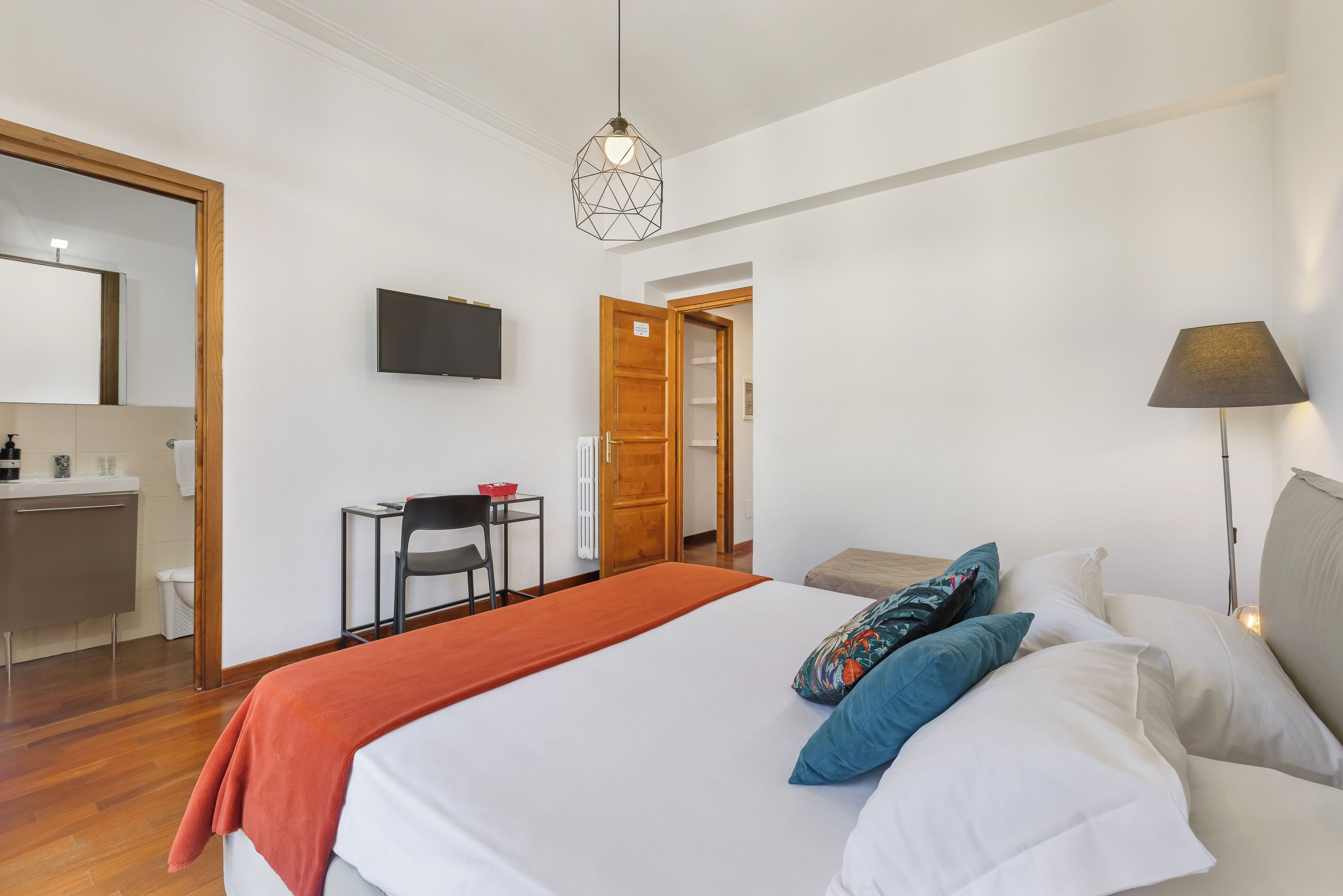 A hotel room with a bed, a desk, a chair, a television, and a door leading to a bathroom.