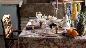 A dining table set with tea service, surrounded by chairs, a window with a view of greenery, and a rustic brick wall. - Bisalde Agroturismo (Bakio)