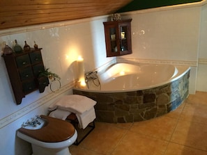 A bathroom with a stone bathtub, a wooden vanity, a toilet, and a cabinet with decorative bottles. - Bisalde Agroturismo (Bakio)