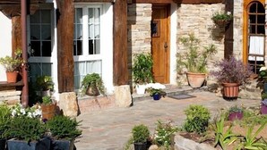A rustic stone house with a tiled roof, wooden columns, and a covered porch with potted plants. - Bisalde Agroturismo (Bakio)