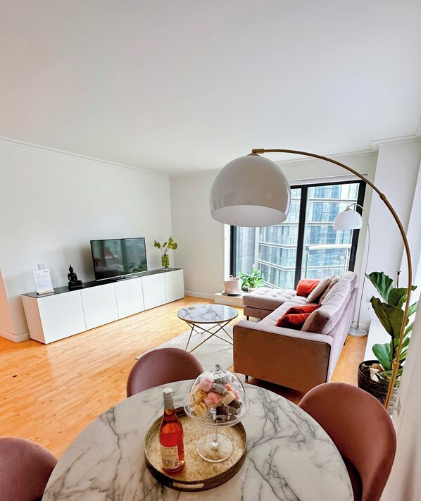 A modern living room with a marble coffee table, a sofa, a TV, and a large window with a view of buildings.