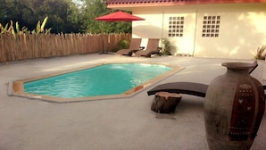 A swimming pool with a wooden deck, a red umbrella, and a rustic vase. - Bamboo Resort (Khanom)