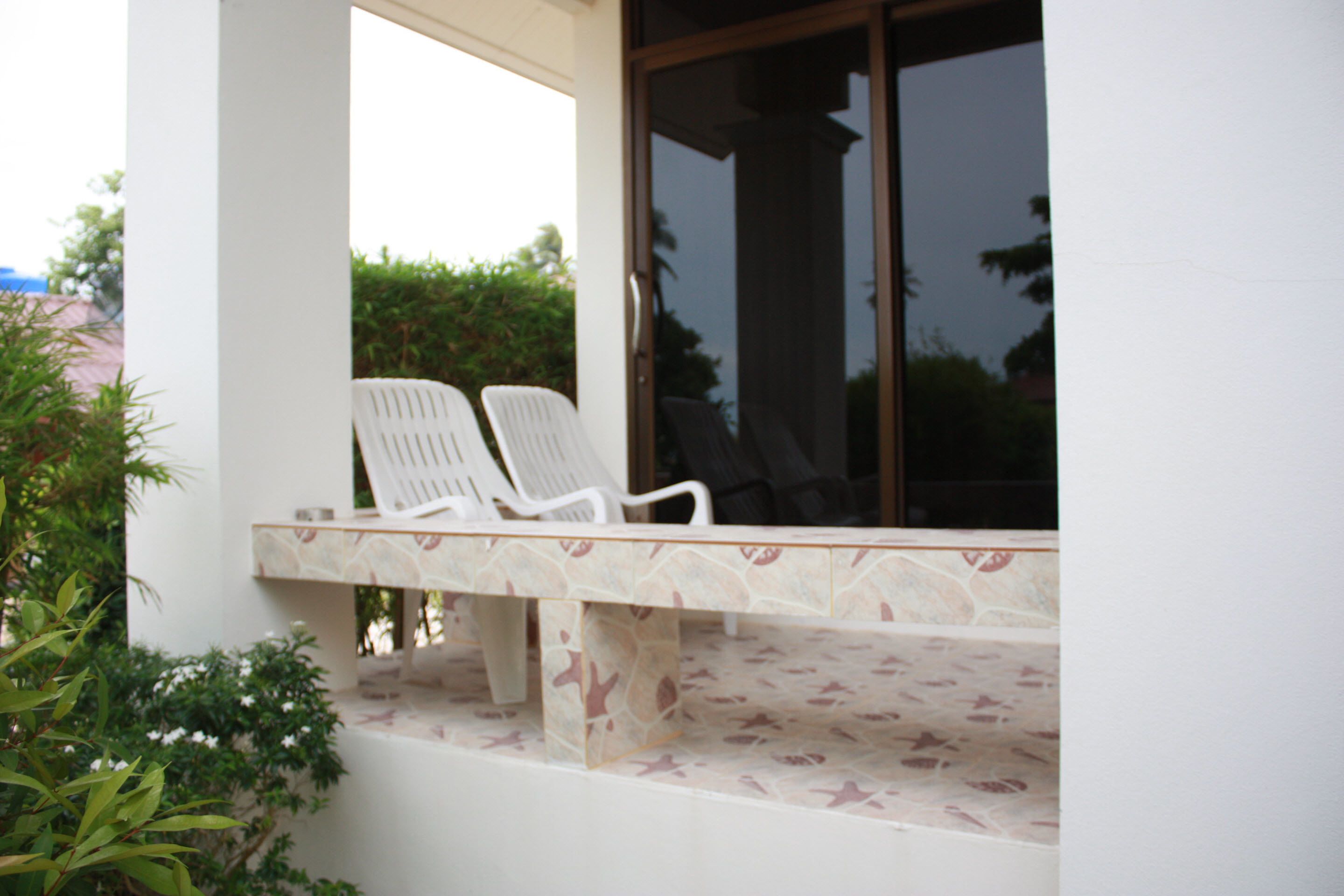 A covered outdoor seating area with two white plastic chairs and a stone-tiled bench.