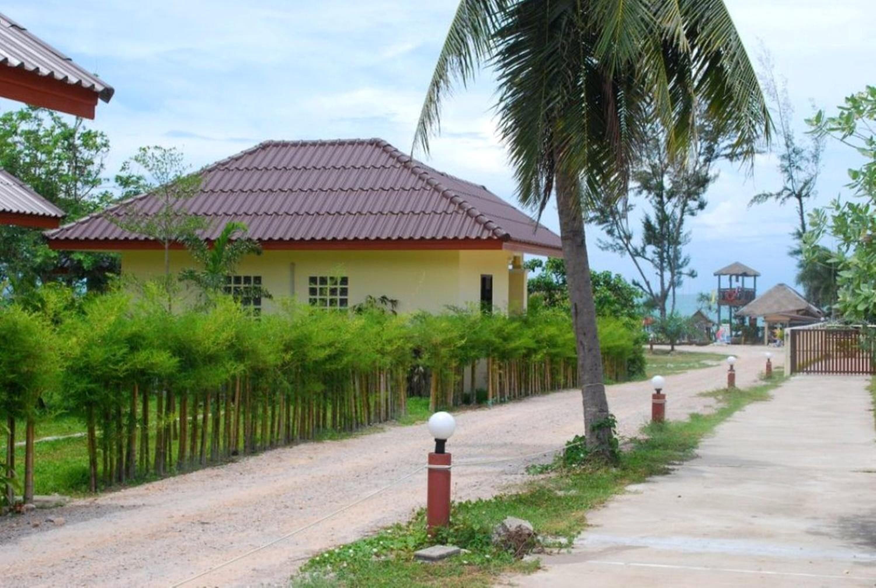A yellow building with a red roof, surrounded by a gravel path and greenery.
