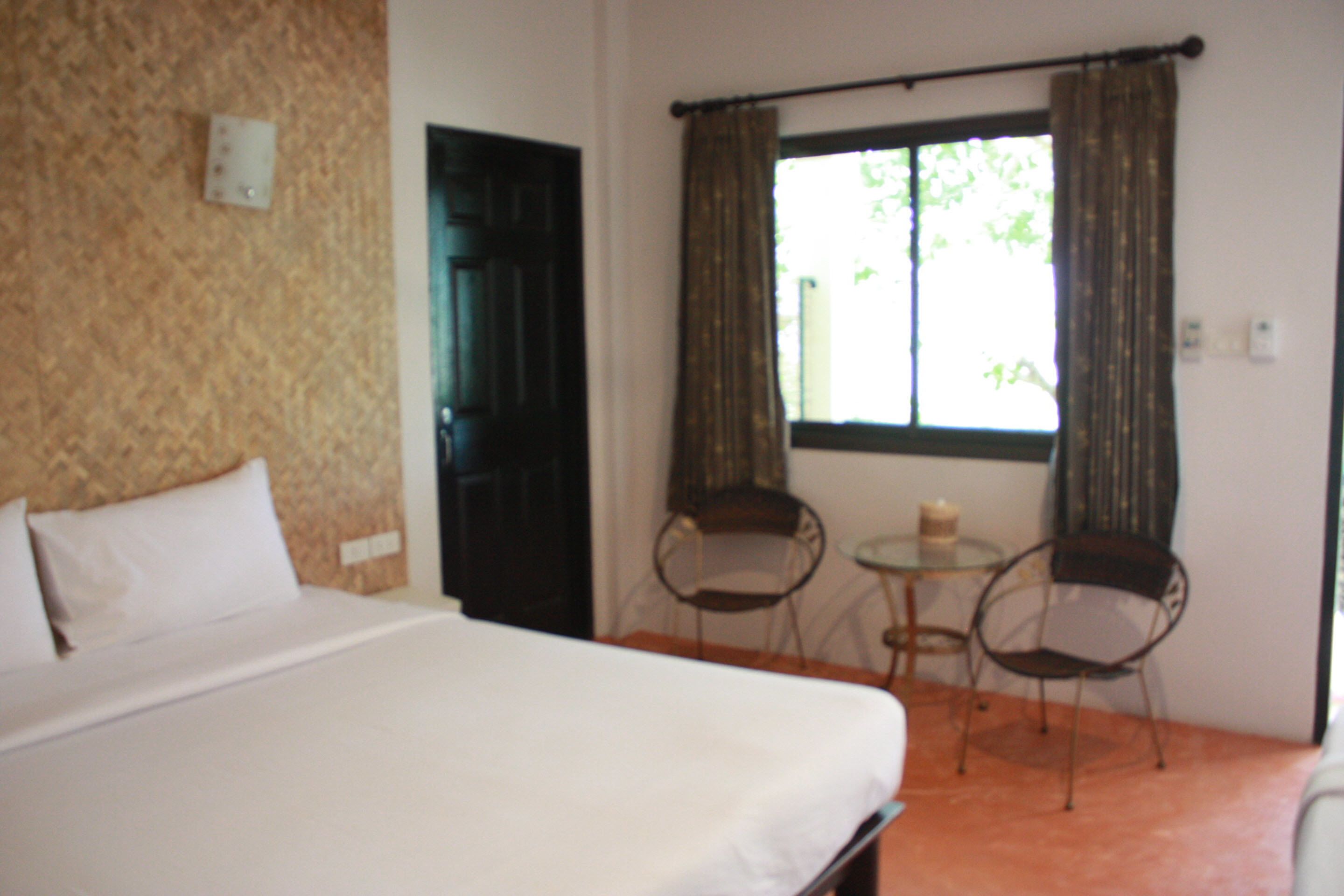 Una habitación con una cama, dos sillas, una mesita y una ventana con cortinas.