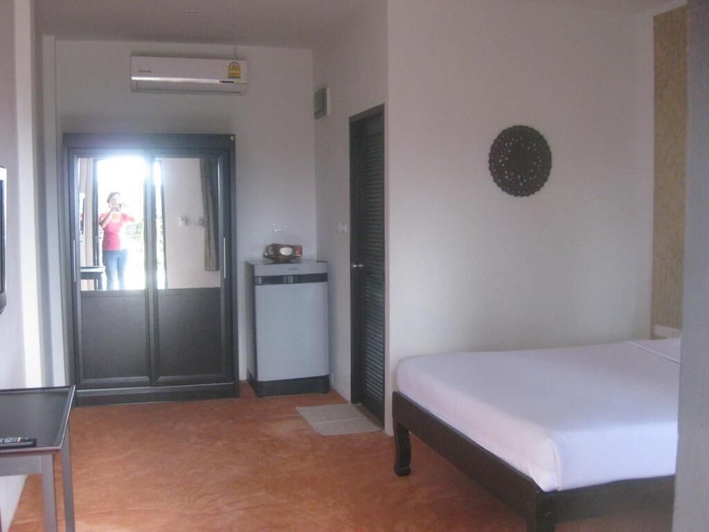 A hotel room with a bed, a desk, a small table, a mirror, a door, and a wall-mounted decoration.