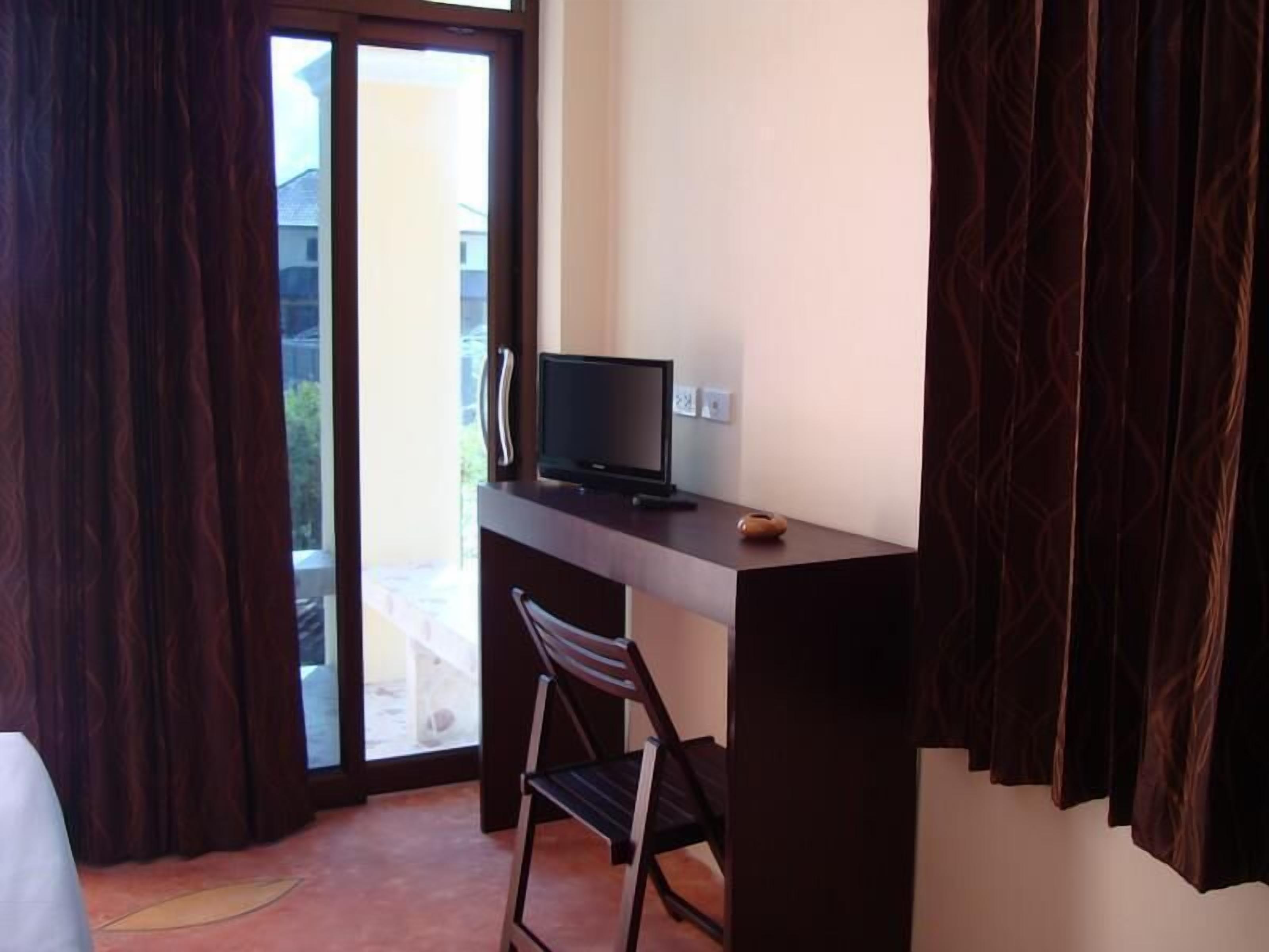 A room with a desk, a chair, a television, and a window with curtains.