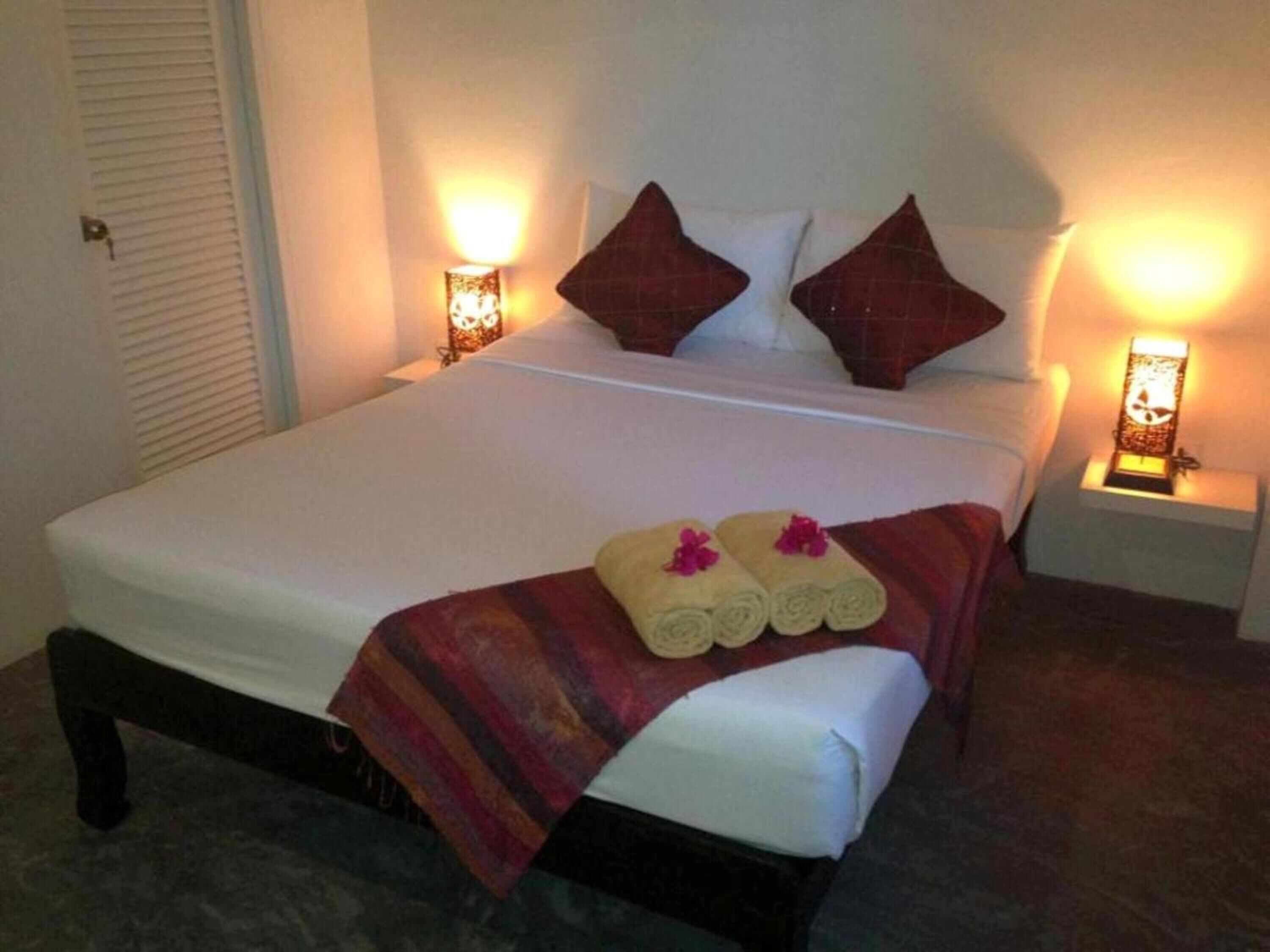 Cama com roupa de cama branca, duas almofadas e um cobertor listrado. Há duas toalhas enroladas com flores sobre a cama.
