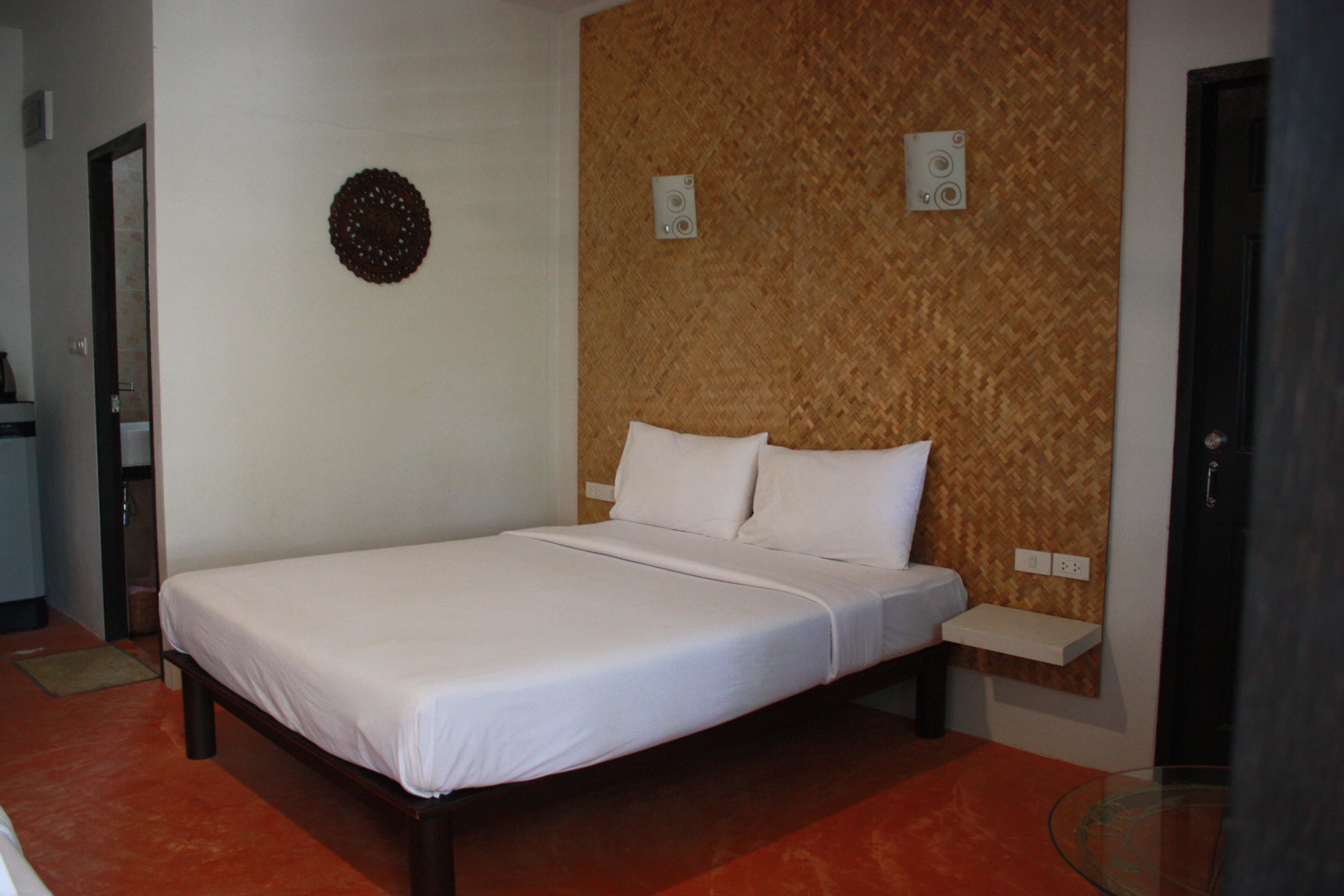 A neatly made bed in a room with a herringbone-patterned wall, a small shelf, and a glass table.