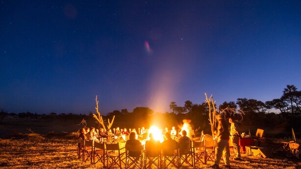 Un grupo de personas reunidas alrededor de una fogata en un campo abierto por la noche.