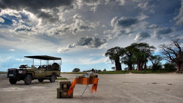 A safari vehicle parked on a dirt road with a table set up nearby, under a cloudy sky. - South Mobile Camp (Nxai Pan National Park)