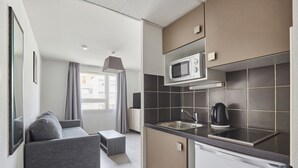 Eine moderne Küche mit Mikrowelle, Wasserkocher und Spüle. Im Wohnbereich befindet sich ein graues Sofa und ein kleiner Tisch.