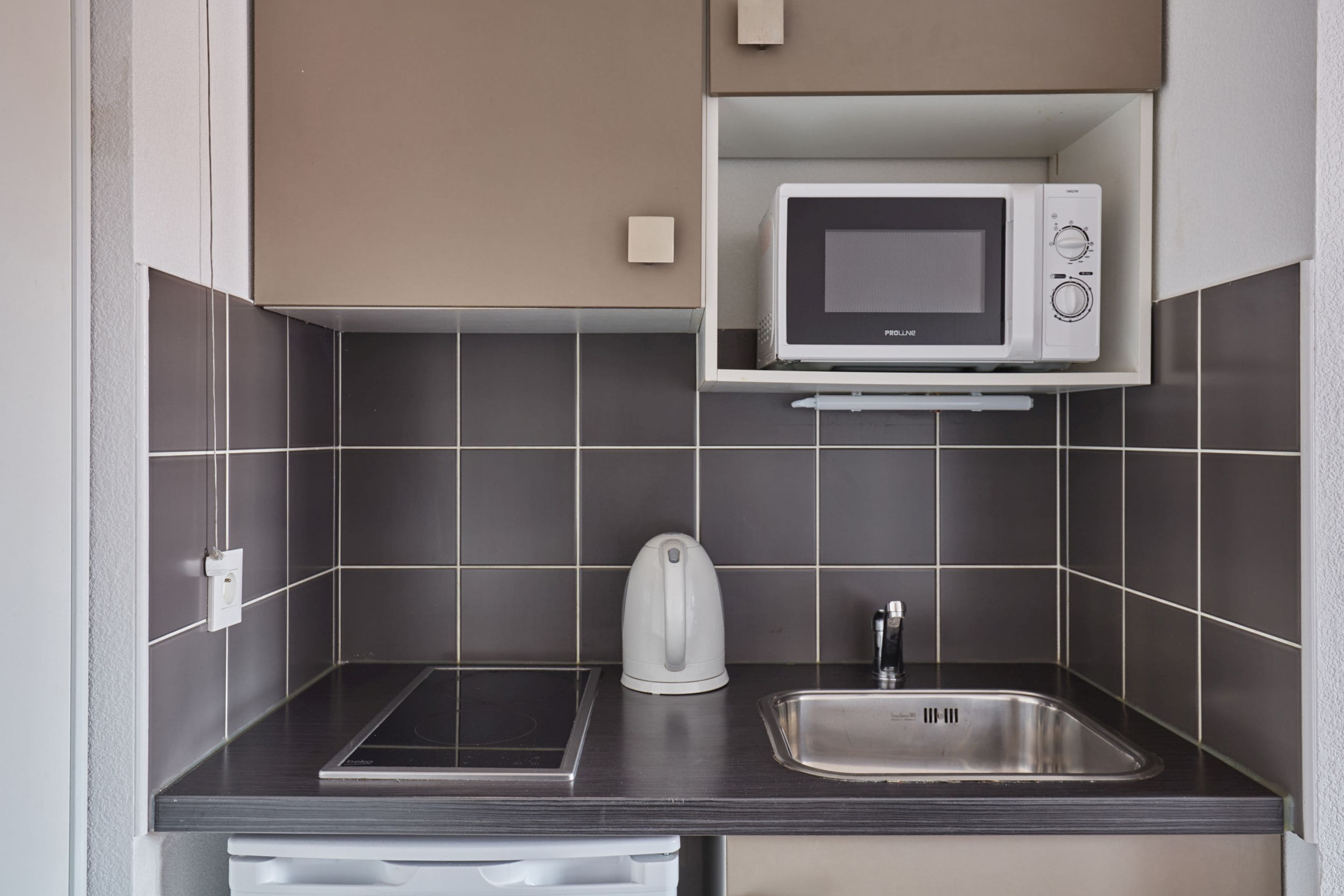 A compact kitchen with a microwave, kettle, and sink.