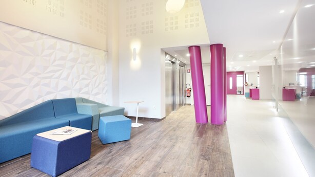 Ein moderner Empfangsbereich mit einem blauen Sofa, einem kleinen Tisch und einer rosa Säule.