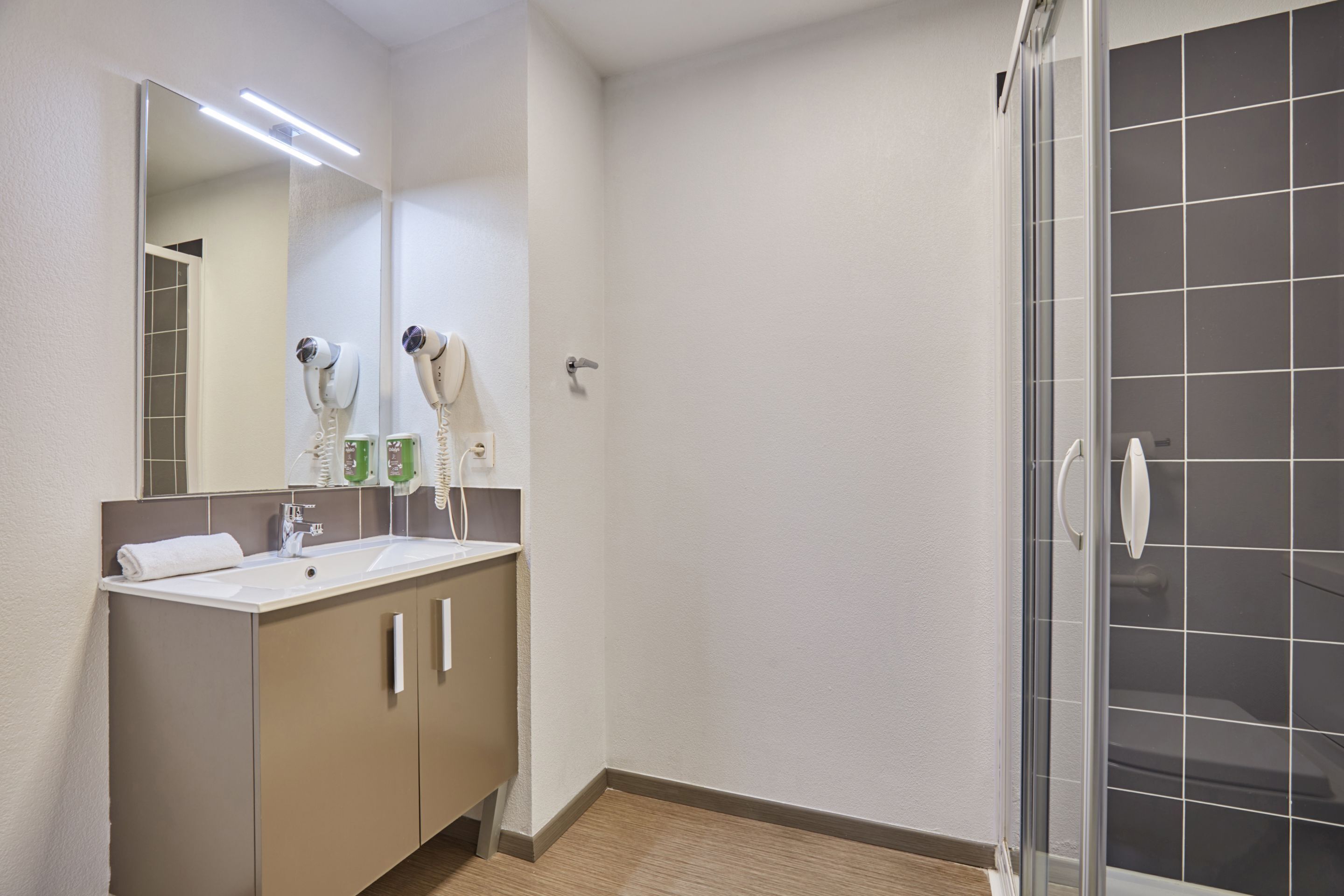 A bathroom with a mirror, two hair dryers, a sink, and a shower area.