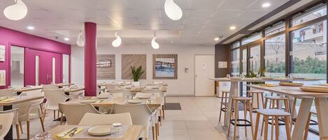 A modern dining area with tables and chairs, a pink wall, and a view through large windows.