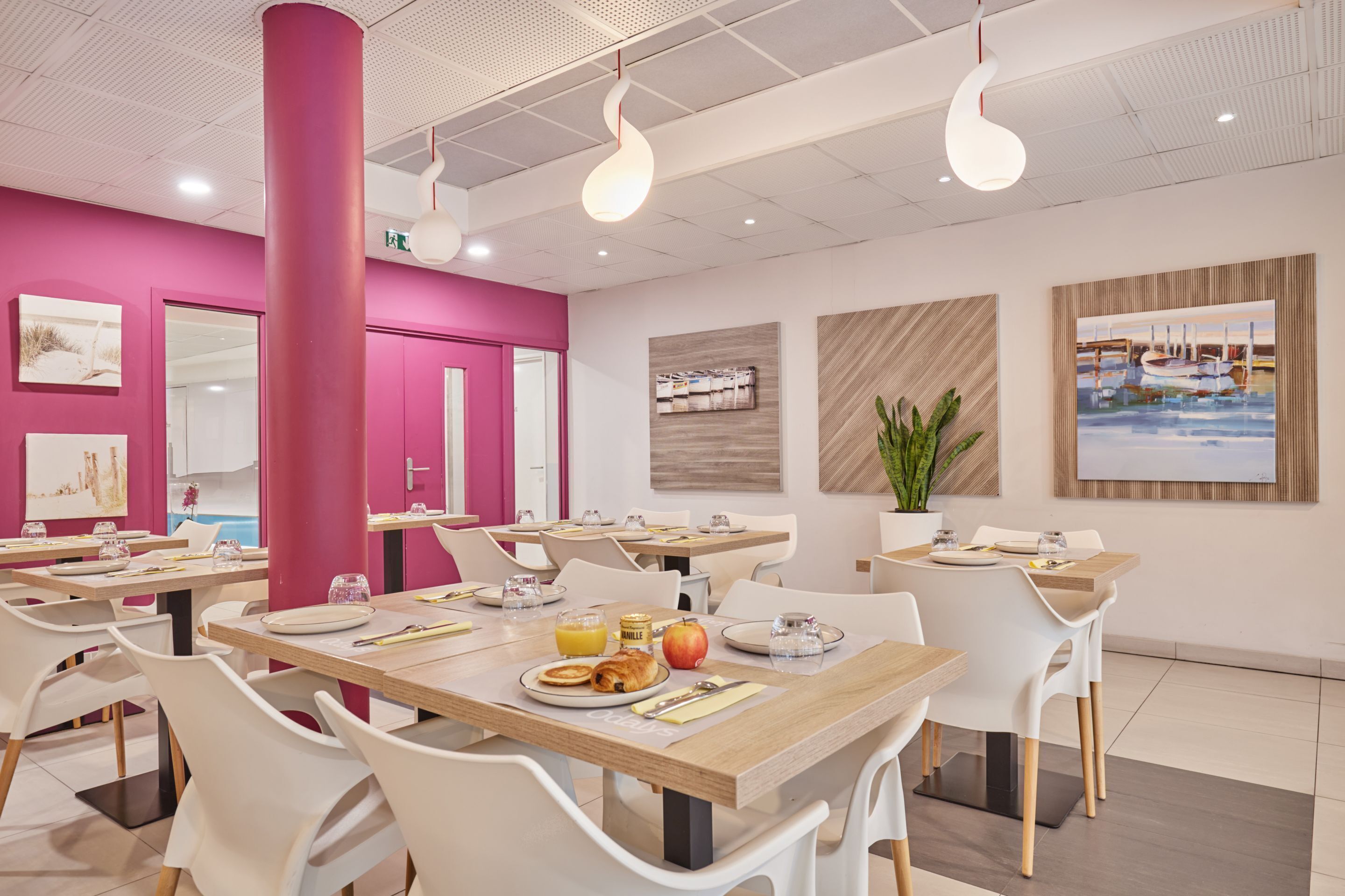 A modern dining area with pink accents, white chairs, and tables set with breakfast items.