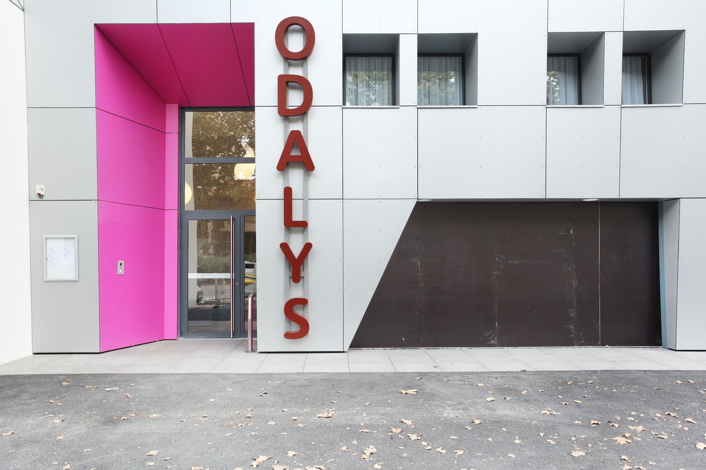 Um edifício com um destaque para o letreiro 'ODALYS', grandes janelas e uma porta de garagem.