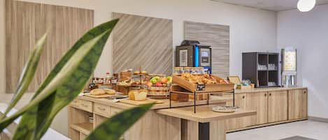 Zona de desayuno tipo buffet con diversas opciones de comida y una máquina de café.