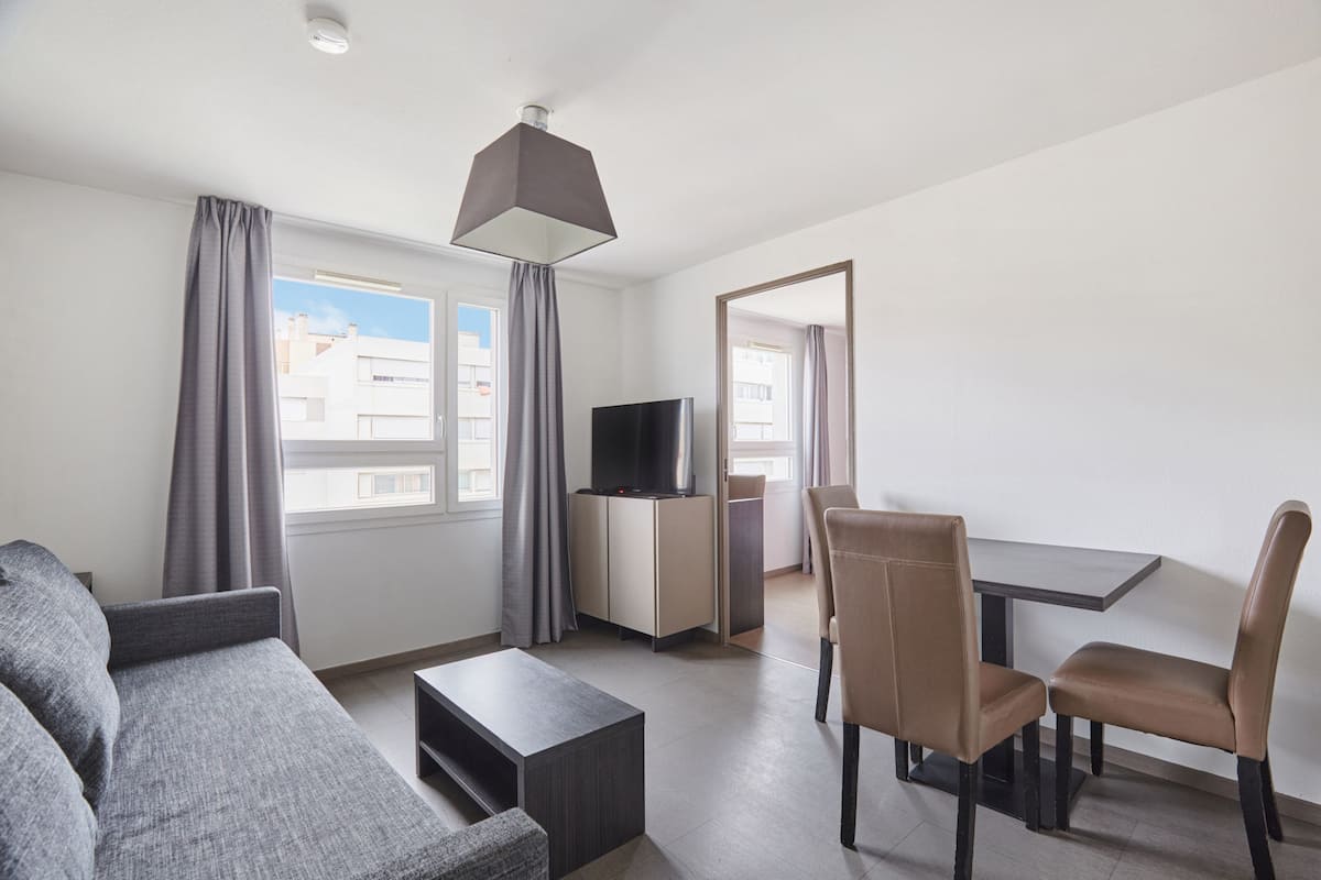 Un salon moderne comprenant un canapé, une table basse, un téléviseur posé sur un meuble et un coin repas avec des chaises et une table.