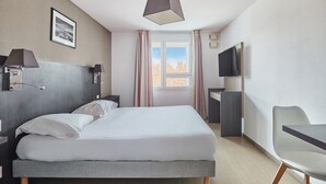 Ein Hotelzimmer mit Bett, Nachttischlampen, Fernseher, Schreibtisch und Stuhl.