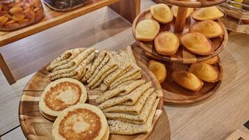 A wooden table with a variety of baked goods, including pancakes and pastries.