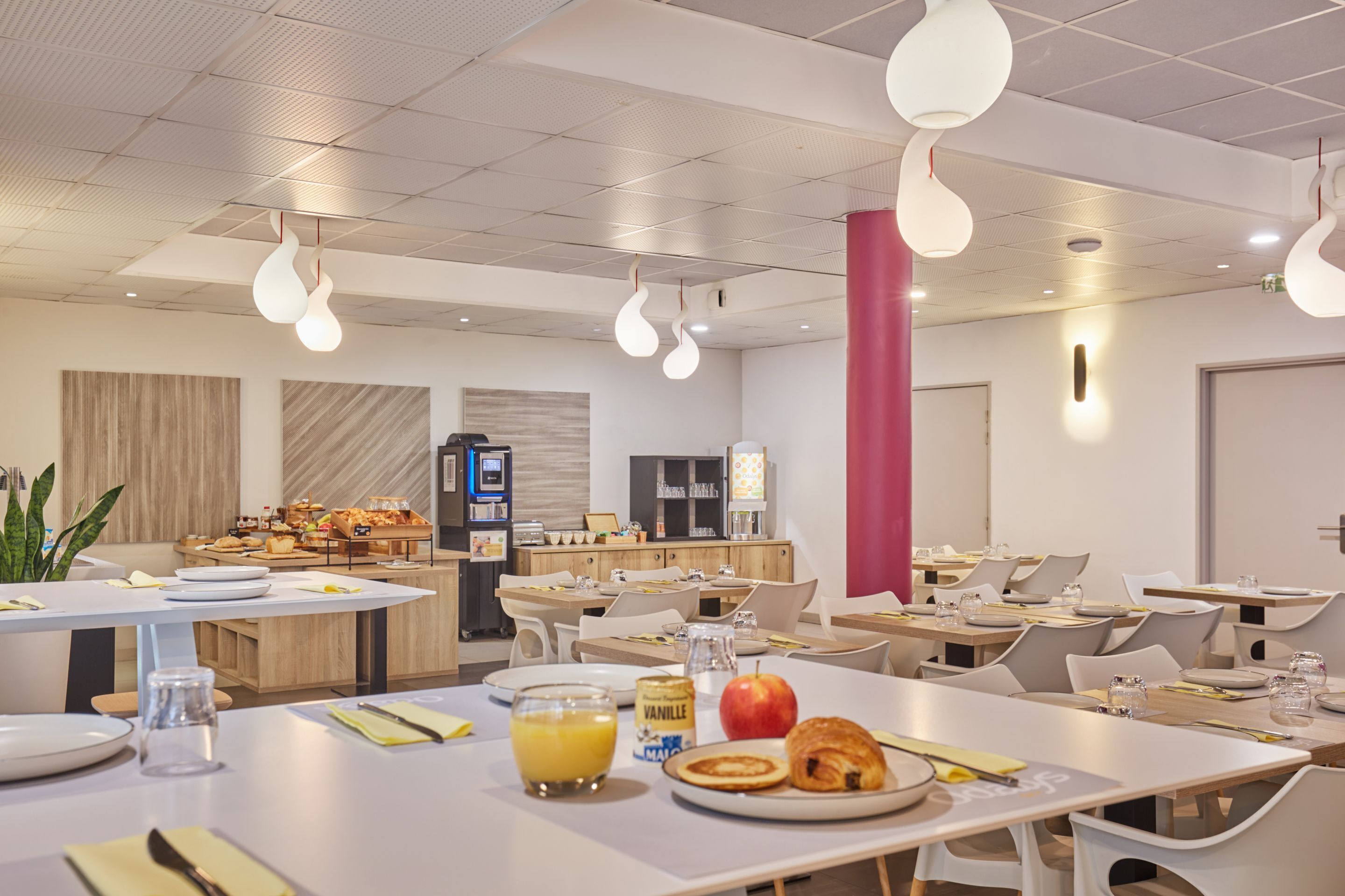 Ein moderner Essbereich mit runden Tischen, weißen Stühlen und einem Frühstücksbuffet.
