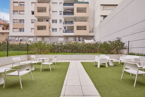 Un patio con mobiliario exterior, un sendero y un edificio con balcones al fondo.