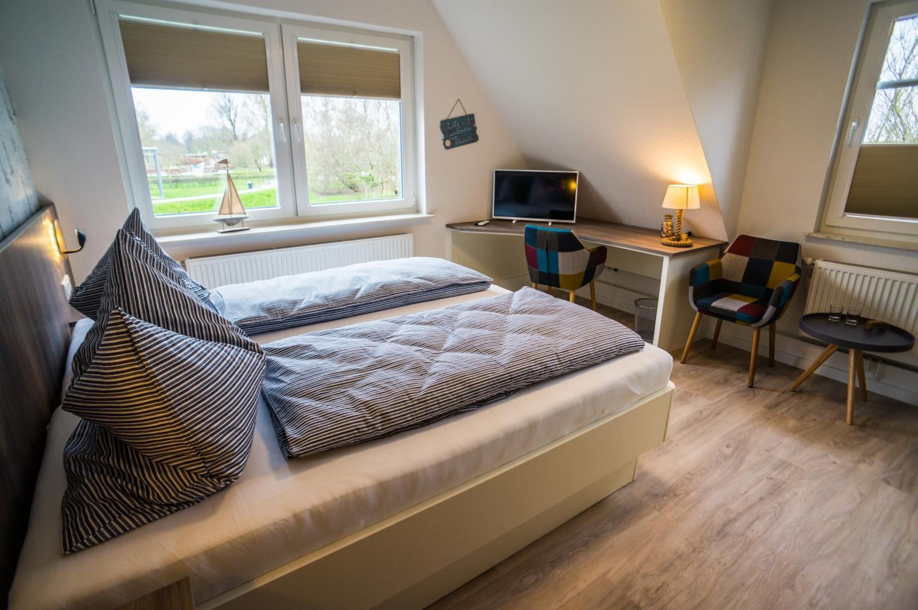 Un dormitorio con cama, escritorio, silla, televisión y ventana.